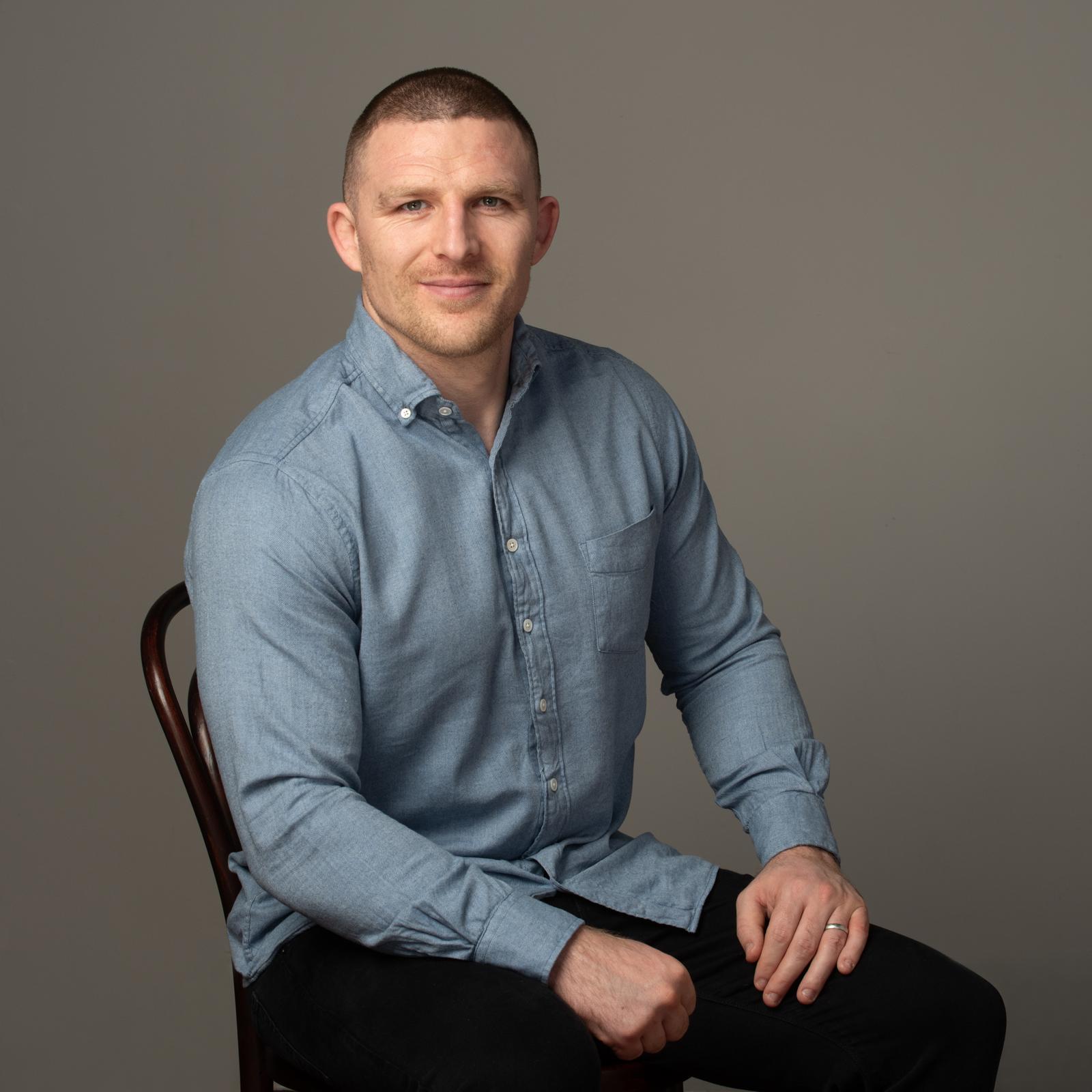 Studio portrait of Andrew Conway, seated, in a blue shirt.